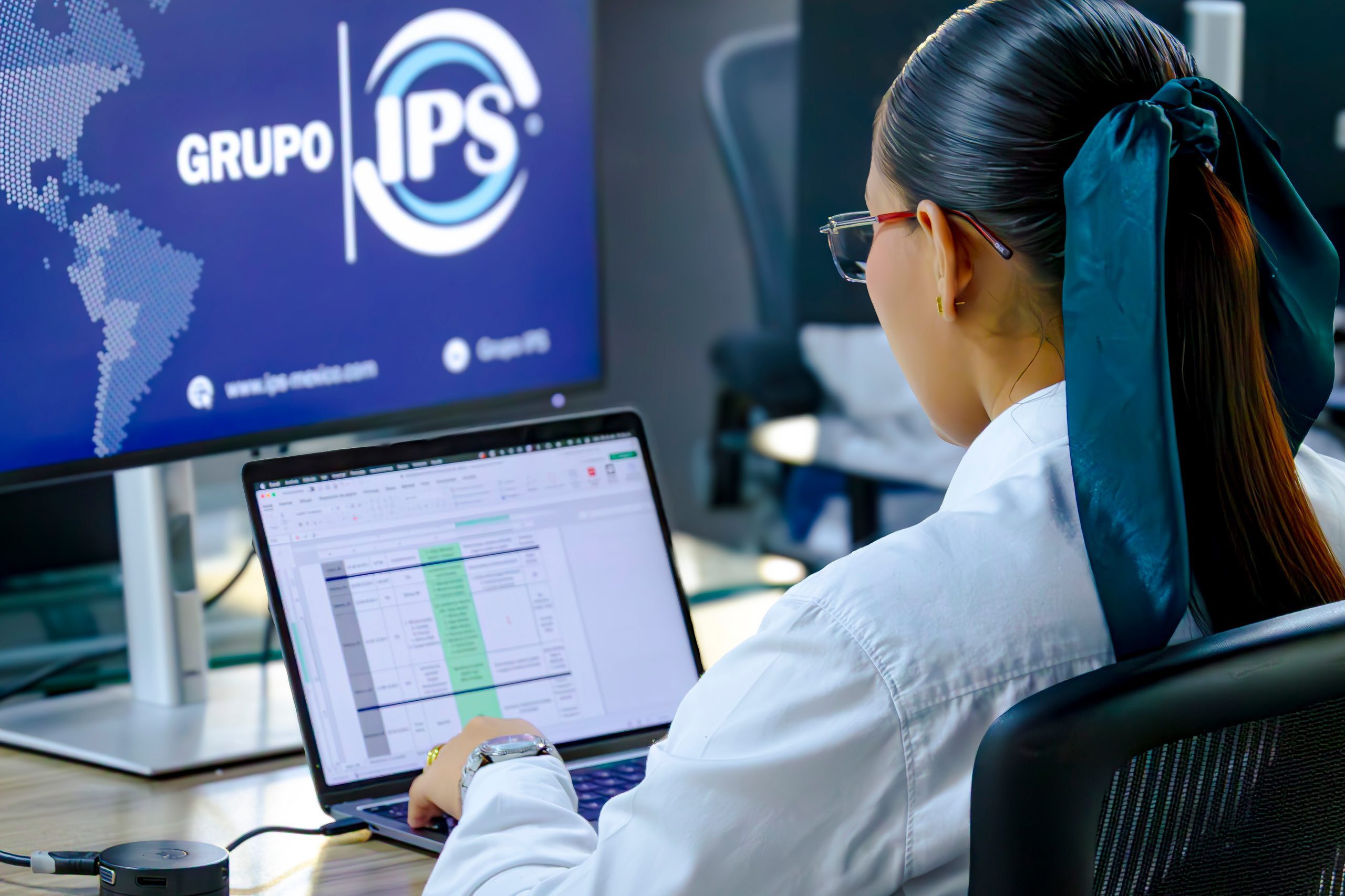Grupo IPS engineer working on a laptop in front of a screen with the Grupo IPS logo