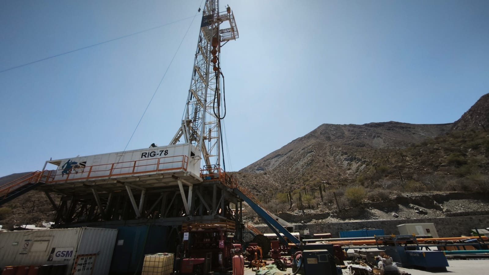 Drilling rig on a geothermal well pad below a rocky mountainside