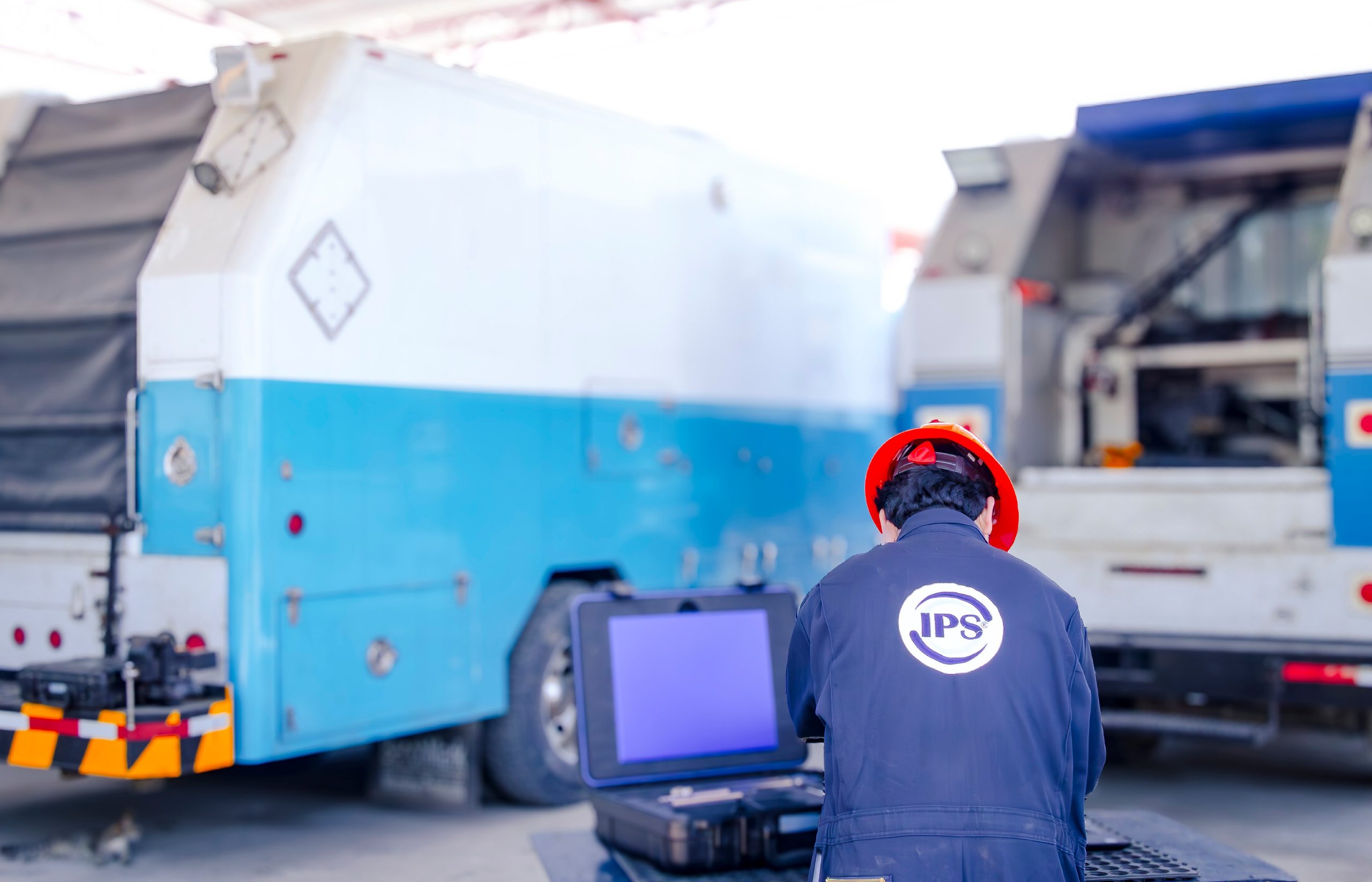 Grupo IPS technician in a red hard hat facing service trucks at a well site